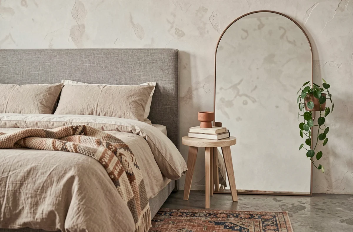 Coin chambre élégant avec tête de lit en lin, miroir arqué en bronze brossé et mur en enduit à la chaux, tendances décoration intérieure apaisante